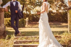 jeune mariée tenant son bouquet la robe à côté de son mari dans les escaliers du parc du château