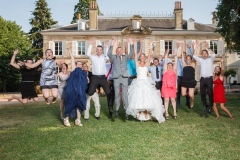 couple de mariés entouré des témoins et amis sautant bras en l'air dans le parc du château de leur mariage