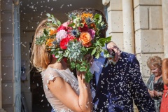 baiser des mariés cachés derrière le bouquet sous une pluie de lavande à la sortie de la chapelle