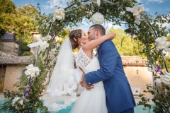 baiser des mariés sous une arche de fleur en extérieur