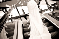 jeune mariée seule dans les escaliers roulants de l'aéroport de Lyon avec une robe à longue traîne avec des plumes