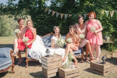 mariée et ses amies souriant assises sur une banquette dans le parc du château de son mariage