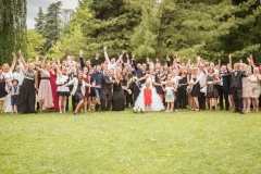 grand groupe entourant les mariés tous bras en l'air dans un parc  de verdure à Voiron