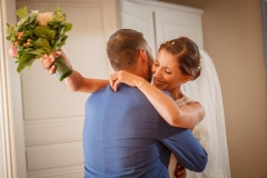 futur marié en costume bleu prenant dans ses bras la future mariée heureuse tenant son bouquet à la main