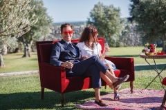 couple avec lunettes fantaisie dégustant une coupe de champagne installé dans un canapé dans le parc du domaine pendant le cocktail du mariage