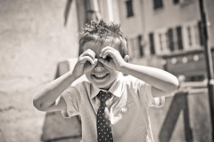 petit garçon en cravate sourit au photographe avec les mains en guise de jumelles autour des yeux