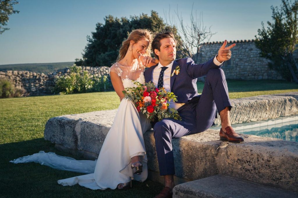 couple de jeunes mariés assis sur le bord d'une piscine prend une pose de statue en riant. contact photographe mariage